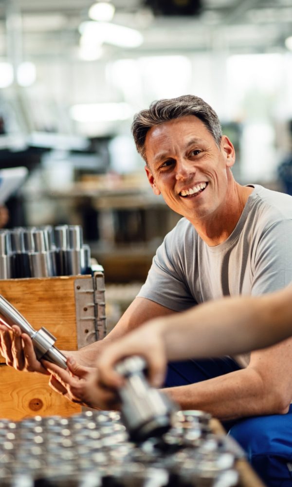 Two happy steel workers preparing manufacture products for the distribution and communicating in industrial facility. Focus is on mid adult worker.